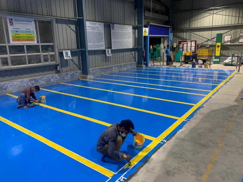 Technicians applying epoxy floor coating in an industrial warehouse